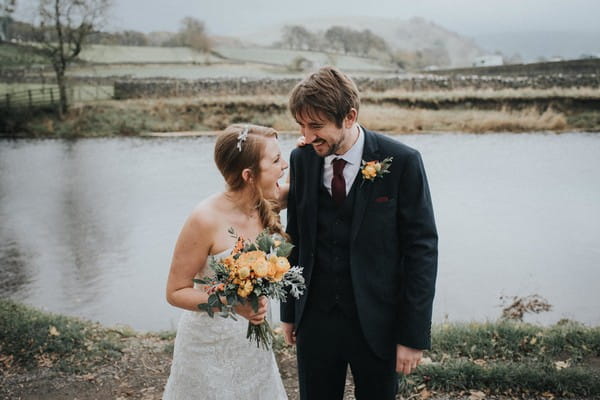 Bride and groom laughing by lake - Picture by Louise Jacob Photography