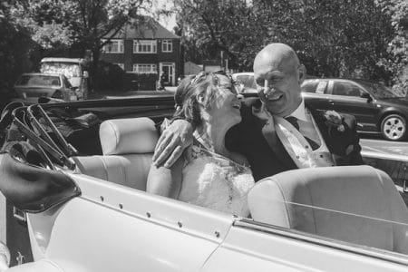 Happy bride and groom sitting in back of convertible wedding car - Picture by Life Through A Lens - Rachel Ellis Photography