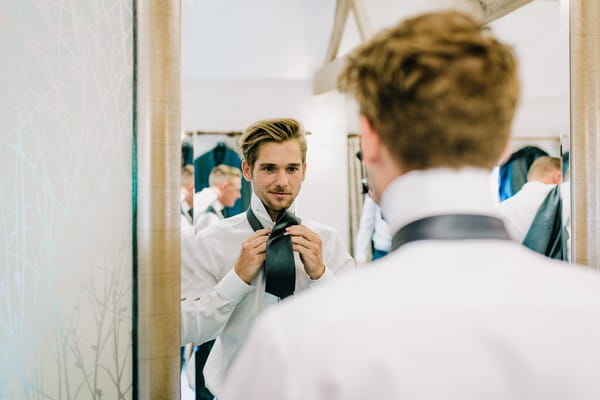 Groom doing tie in mirror