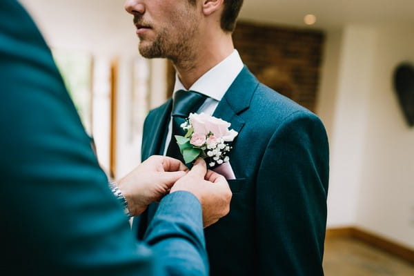Groomsman helping groom with buttonhole