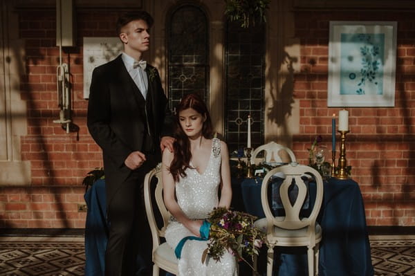 Groom standing next to bride sitting in front of wedding table