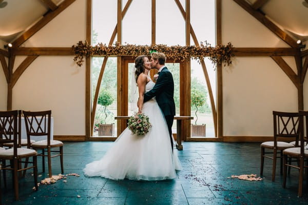 Bride and groom kissing in ceremony room at Mythe Barn