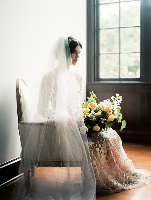 Bride sitting in chair holding bridal bouquet with yellow flowers