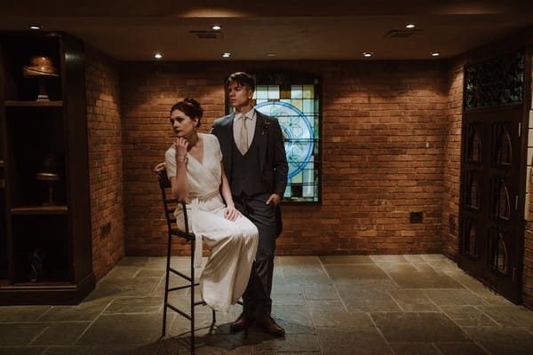 Groom standing next to bride sitting in chair in dark room