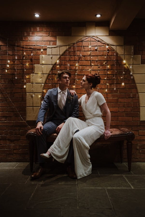 Bride and groom sitting in front of wall of fairy lights