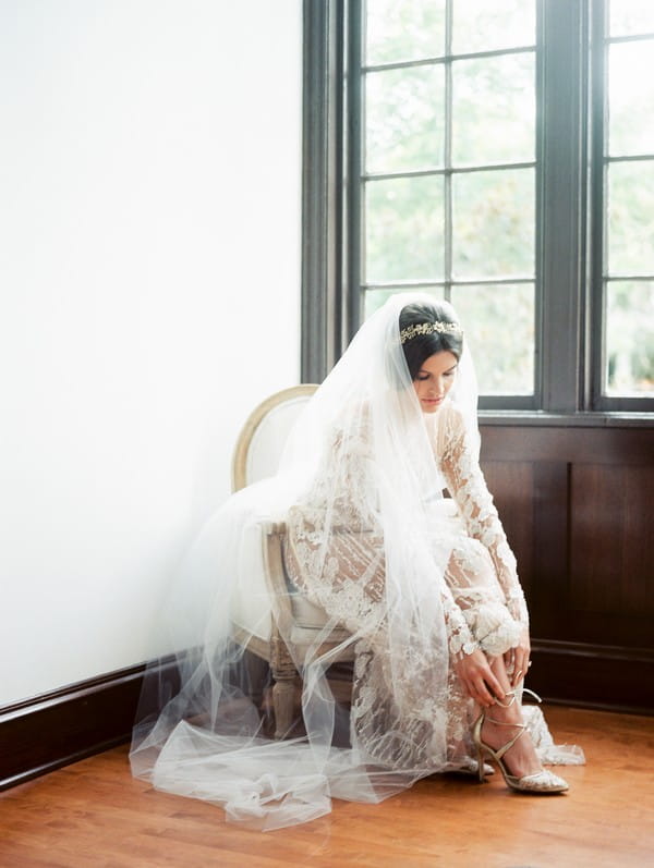 Bride sitting in chair putting on bridal shoes