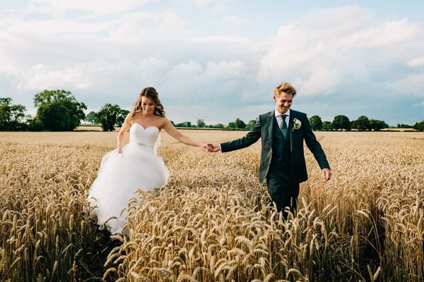 Bride and groom holding hands as they walk through cornfield