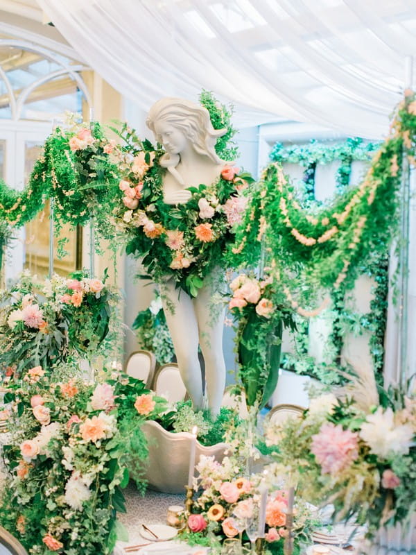 Statue covered in flowers and foliage in centre of wedding table