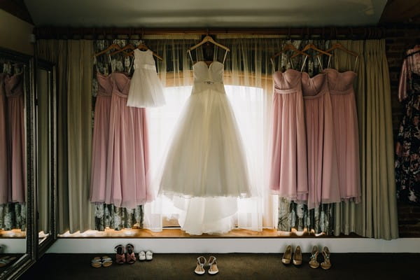 Wedding dress and pastel pink bridesmaid dresses hanging in front of window