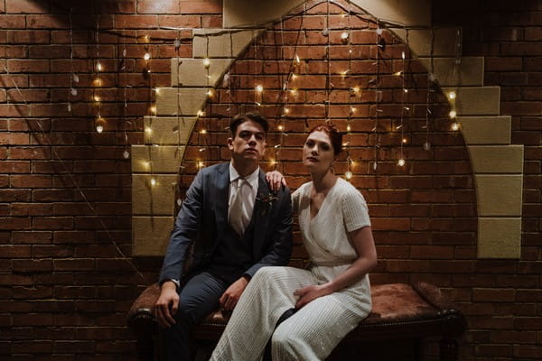 Bride and groom sitting in dark room in front of fairy lights