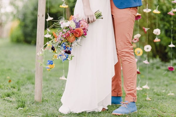 Bride holding colourful bouquet next to groom's coral trousers