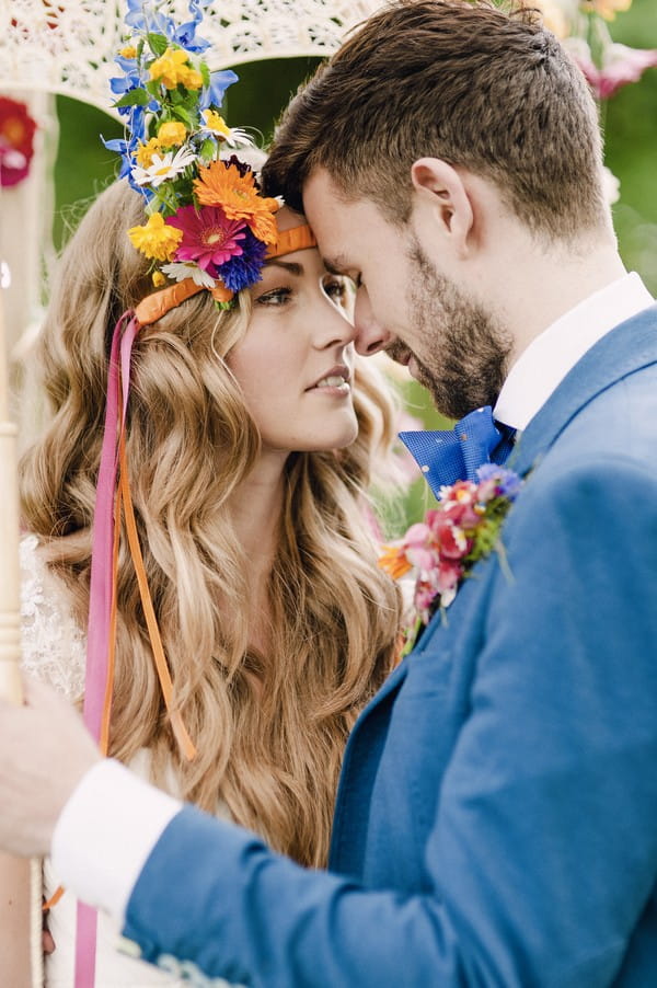 Boho bride with colourful floral headband touching heads with groom