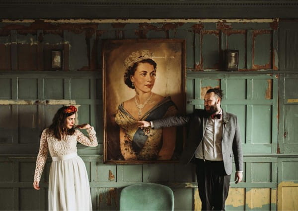 Groom pointing at bride as they stand by picture of the Queen - Picture by Luke Hayden Photography