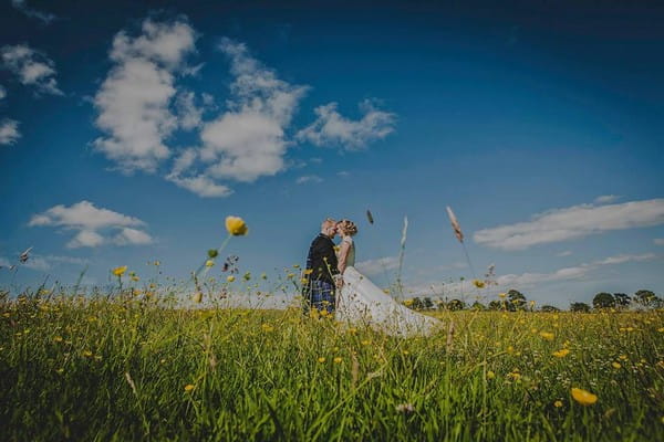 Bride and groom standing in a field of buttercups - Picture by Mike Cook Photography