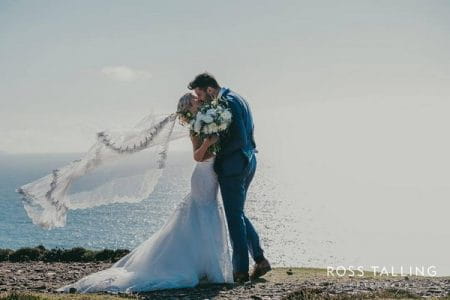 Bride and groom kissing by sea with bride's veil blowing in wind - Picture by Ross Talling Photography