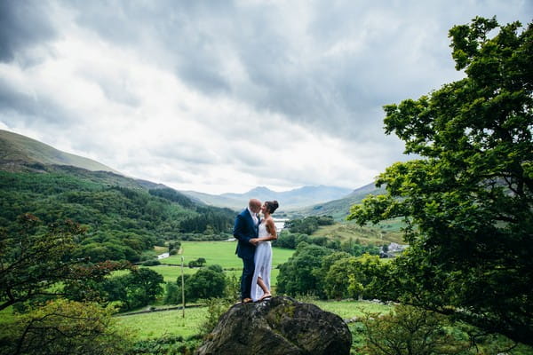 Bride and groom standing on rock with beautiful countryside behind them - Picture by Simon Biffen Photography