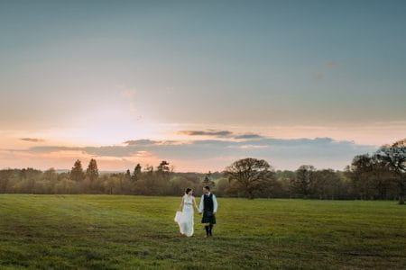 Bride and groom walking holding hands across a field - Picture by Eilidh Robertson Photography