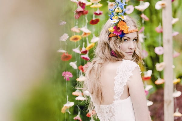 Boo bride looking over her shoulder in front of colourful suspended floral backdrop