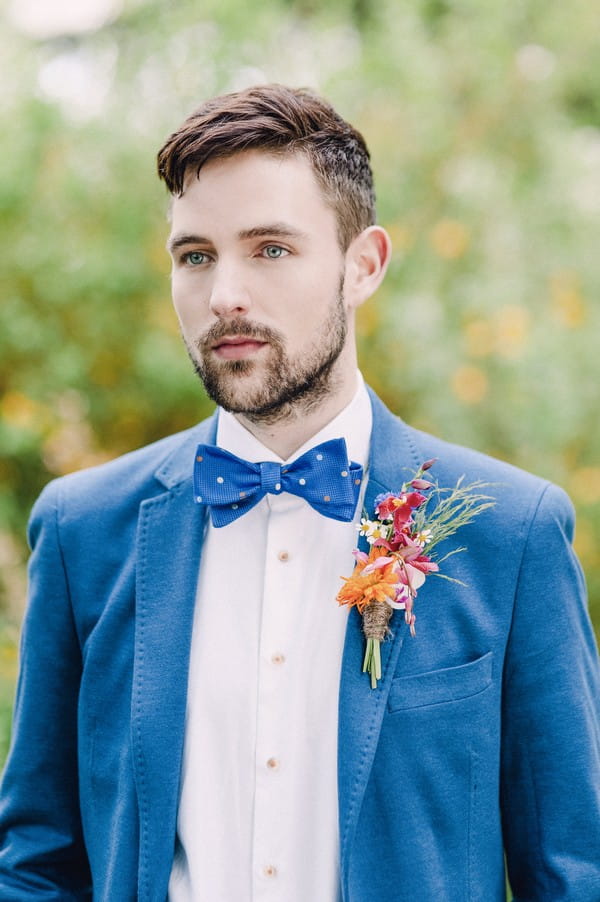 Groom wearing blue jacket and bow tie with colourful buttonhole