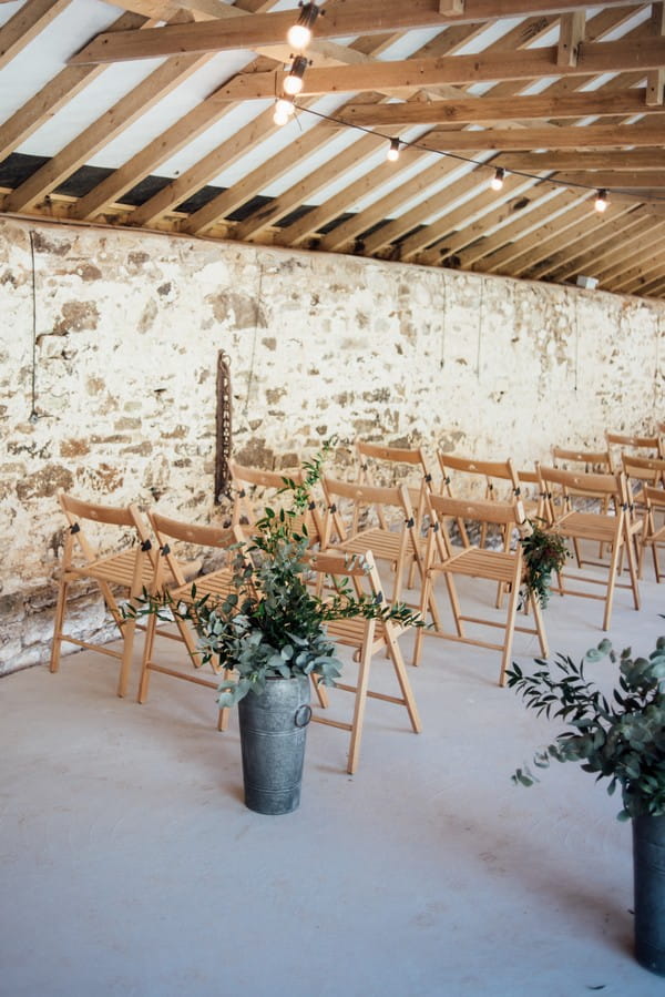 Urns of foliage in front of rustic wedding ceremony chairs