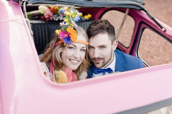 Bride and groom looking out of sunroof of pink car