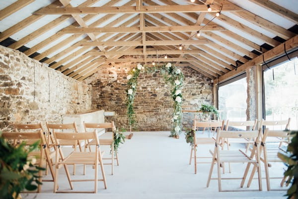 Flower and foliage arch at end of wedding ceremony aisle in The Cowyard Barn at Pengenna Manor