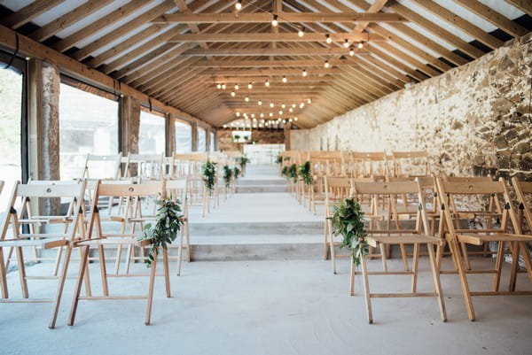 Rustic chairs lining ceremony aisle at The Cowyard Barn at Pengenna Manor