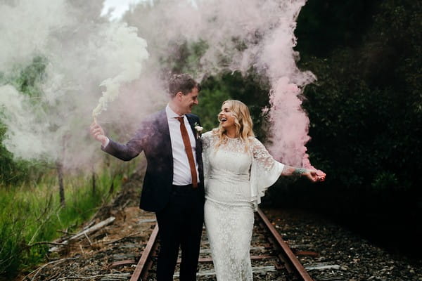 Bride and groom on train track holding smoke bombs