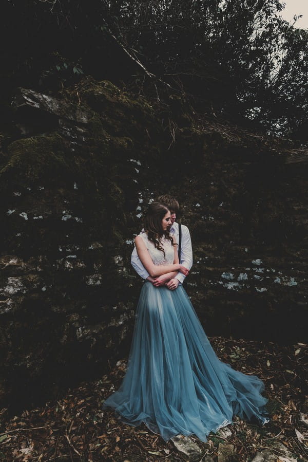 Groom hugging bride wearing blue skirted dress from behind