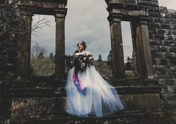 Bride holding bouquet by pillars in Goyt Valley