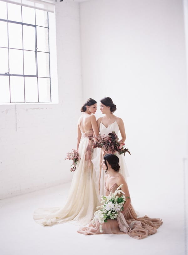 Three brides wearing blush and white dresses, holding bouquets