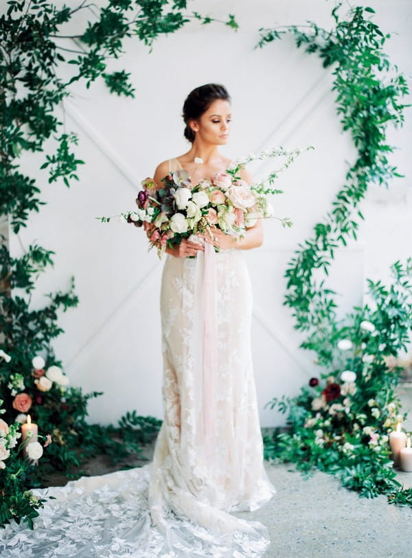 Bride holding bouquet in front of foliage backdrop