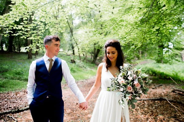 Bride and groom holding hands as they walk through woodland - Picture by Nicola Norton Photography