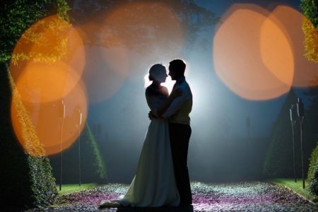 Bride and groom on path at night with light shining behind their heads - Picture by Photography by Suzanne Fossey