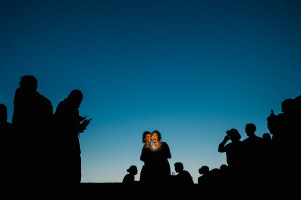 Two brides surrounded by silhouettes of wedding guests - Picture by Emma and Rich