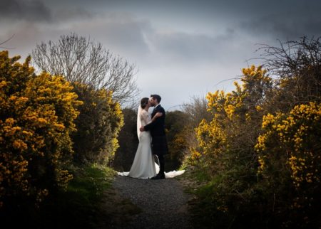 Bride and groom kissing on path surrounded by bushes - Picture by Giles Atkinson Photography