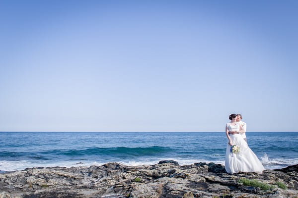 Bride and groom standing on rocks by the sea - Picture by Brian Robinson Photography