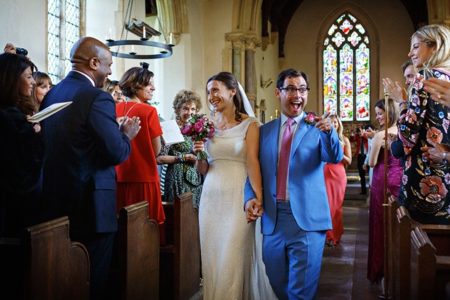 Groom pointing at wedding guest with big smile on his face as he leaves wedding ceremony with bride - Picture by Duncan Kerridge Photography