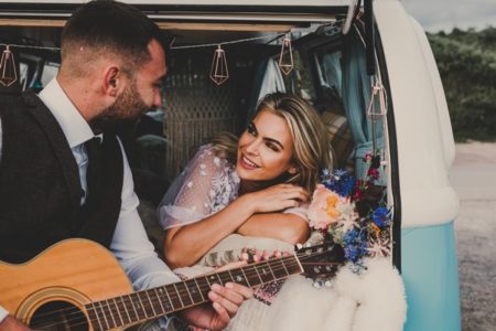 Bride sitting on back of camper van as groom plays guitar - Picture by Jade Maguire Photography