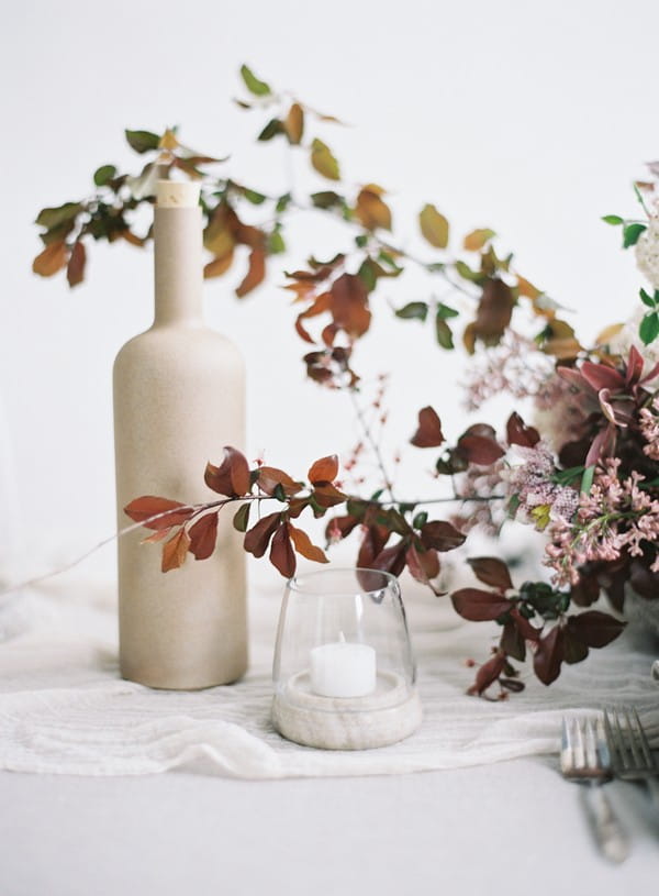 Candle, bottle and red leaves from floral wedding table display