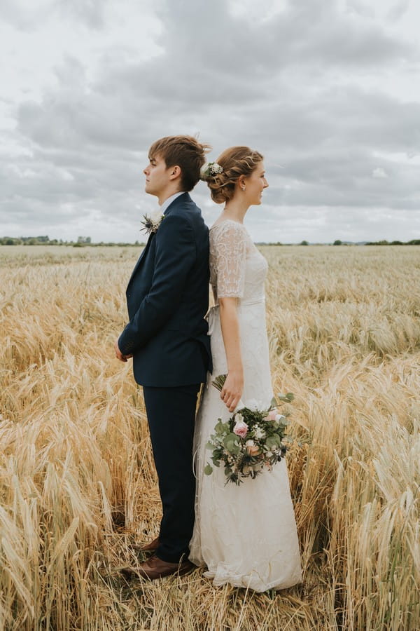 Bride and groom standing back to back in cornfield