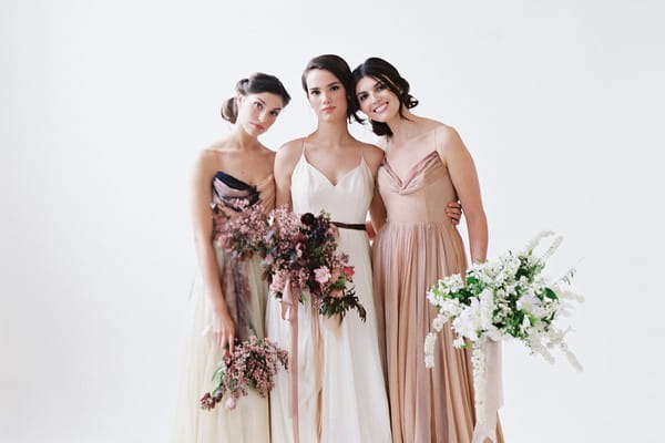 Three brides in white and blush wedding dresses holding bouquets