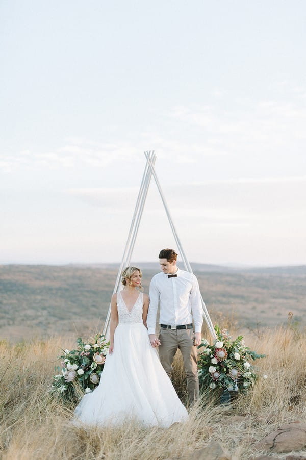Bride and groom standing in front of tipi style ceremony arch