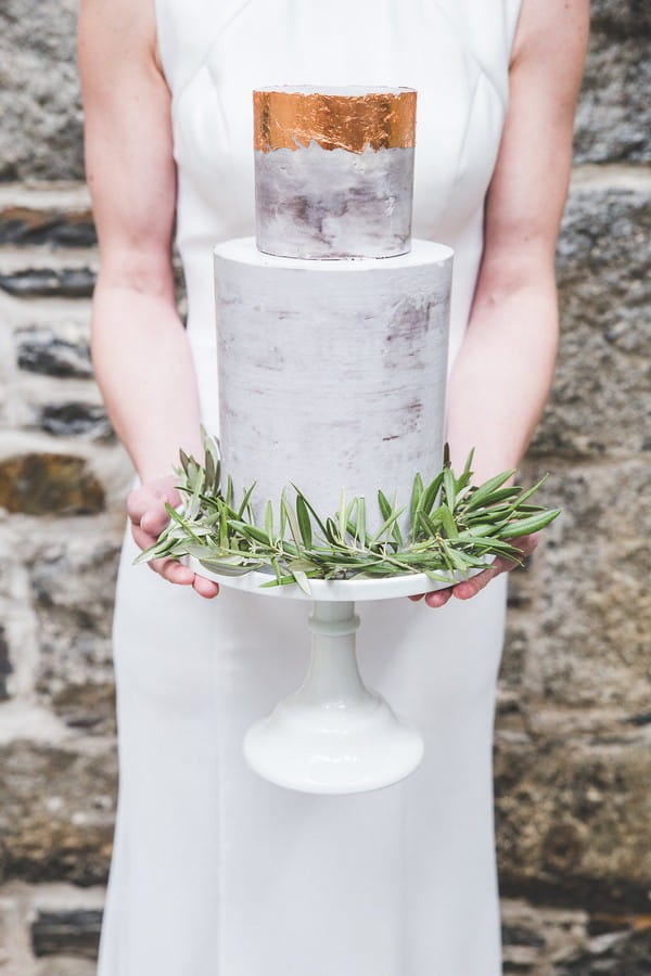 Bride holding wedding cake with copper top and rosemary around base