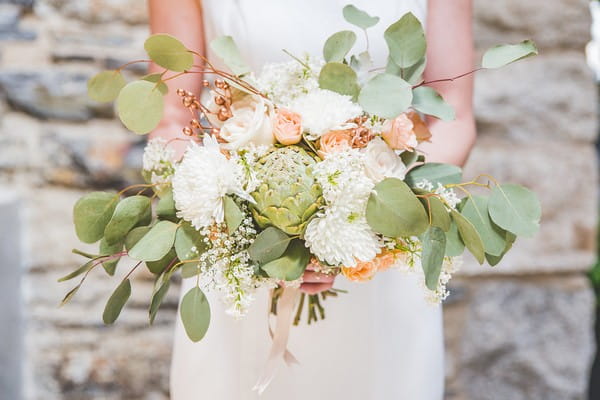 Bride holding peach, white and green bouquet with artichoke