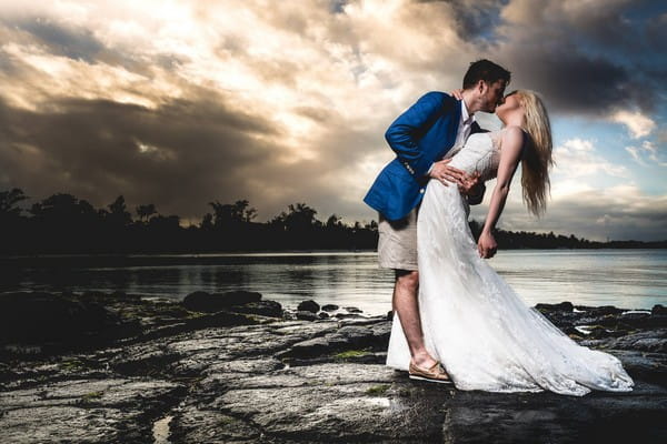 Groom in shorts kissing bride on rocks by water - Picture by Tony Boyle