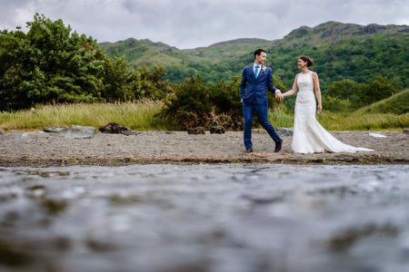 Bride and groom walking holding hands with hills in background - Picture by Cris Lowis Photography