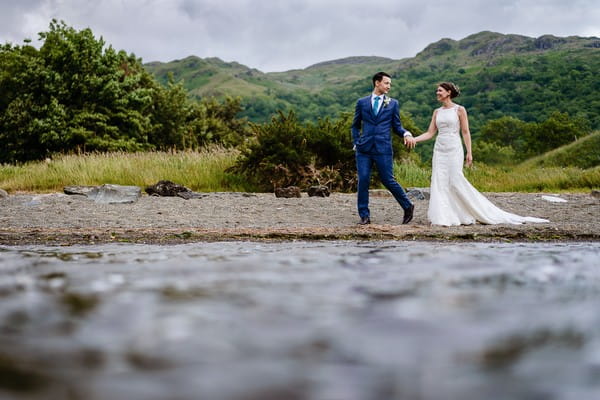 Bride and groom walking holding hands with hills in background - Picture by Cris Lowis Photography