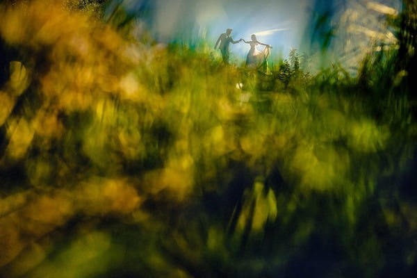 Picture taken through grass of bride and groom on a hill - Picture by Steven Rooney Photography