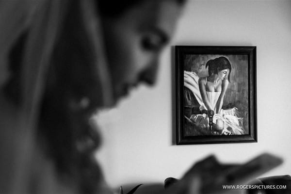 Bride looking at phone with picture of lady on wall in background - Picture by Paul Rogers Photographer